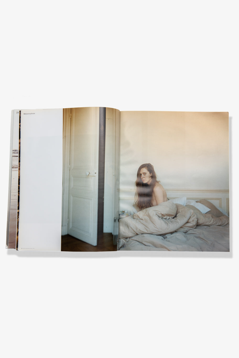 Photograph of a spread of Alec Soth's Paris Minnesota. Recto: A female-appearing model sits on an unmade bed, hair and bedspread covering her partially exposed body. Verso: An open doorway. 