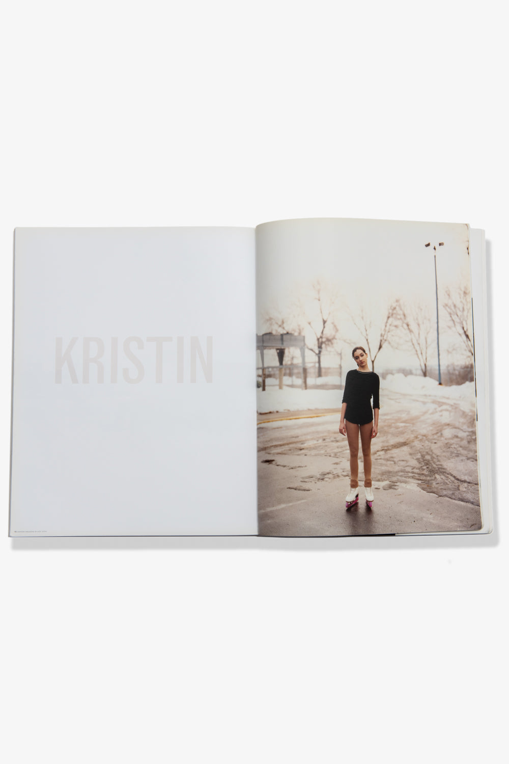 A photograph of a spread of Alec Soth's Paris Minnesota. Recto: A model in an ice skating uniform and skates stands outside on the icy parking lot, likely somewhere in Minnesota. Verso: The name "KRISTIN" printed in pale color against a white page.