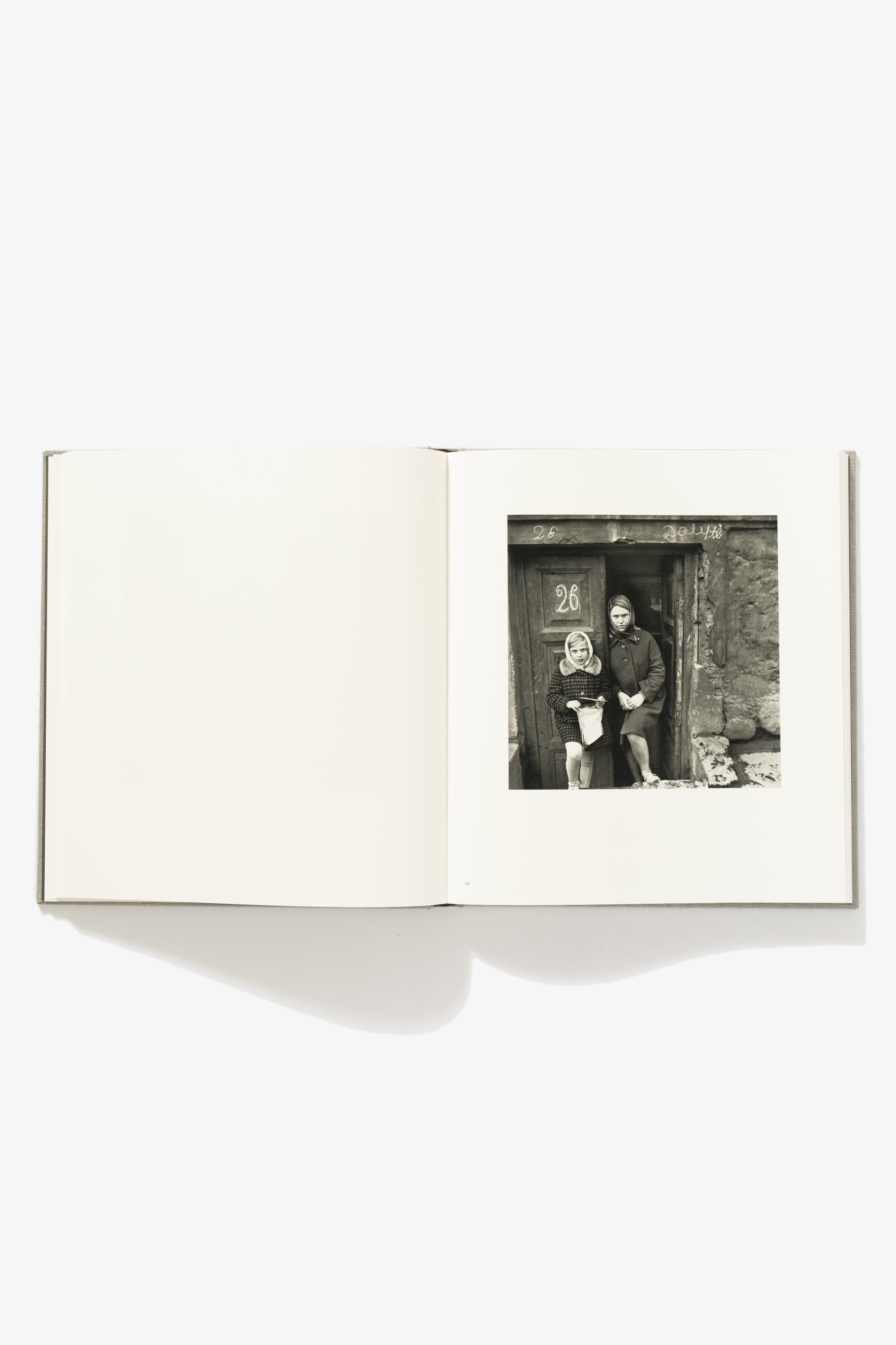 Spread of Antanas Sutkus's "People of Lithuania. Verso is blank. Recto is an image of two girls posing in the doorway. 