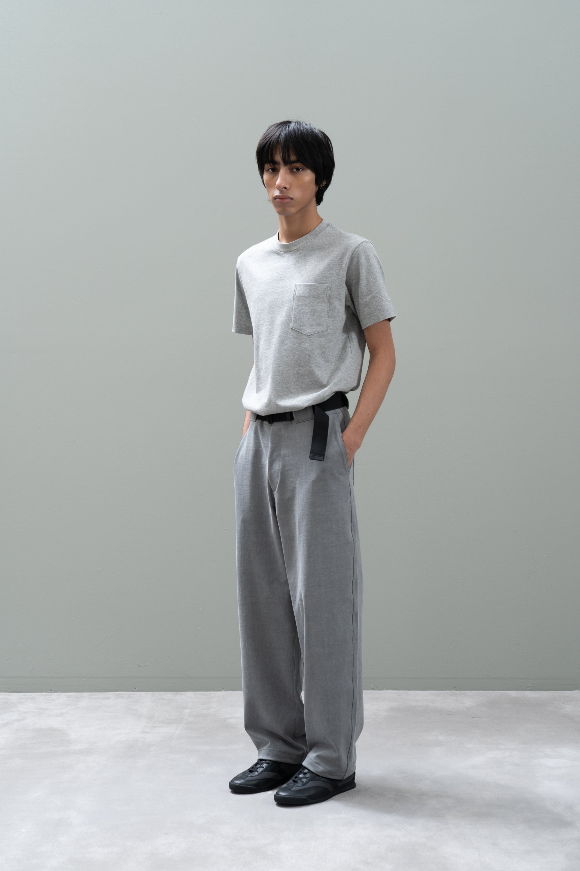 Person wearing a gray t-shirt and pants standing against a plain background